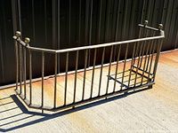 Full angled view of brass and iron fireplace fender showing faceted shape and finials