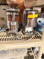 Front view of two Mazzer Mini Timer grinders on shelf showing stainless housings, hoppers, cords