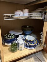 Cabinet view showing majority of ceramic bowls, plates, mugs and green glass piece