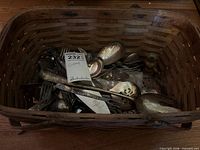 Basket containing assorted tarnished silverplate and stainless cutlery, serving utensils, small candlestick