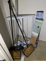 Two leopard print carpet sweepers, white folding closet organizer frame parts, boxed shelf kit visible against wall