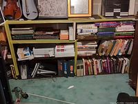Full view of bookcase with books, frames, violin case