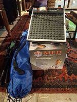 Unboxed MED foot massager on top of original box alongside camp chairs