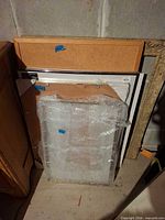 Stack showing cork board on top of several frames, bubble-wrapped frame visible