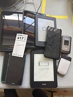 Stack of three tablets, two Kindle e-readers, two smartphones and two flip phones on tabletop