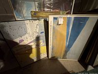 Front view showing two framed posters: blue/yellow abstract and paint-splatter Consort print, plus additional print behind