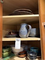 Cabinet shelves holding blue stoneware pitcher, matching bowl, assorted ceramic bowls, and two wicker baskets