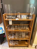 wooden rack holding assorted clear and frosted glass pitchers, vases, glasses, bowls and small accessories