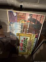Stack of three framed posters leaning against wall, plastic-wrapped
