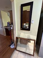 Tall dark brown framed mirror mounted on wall, light brown framed mirror leaning below