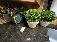 Two faux boxwood arrangements in beige terracotta pots and mixed floral arrangement in dark green ceramic planter