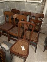 Seven wooden chairs with cane seats stacked together in basement