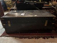 Front view of closed black wood steamer trunk with brass hardware