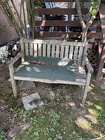 Full view of weathered gray wooden bench with green mat outdoors