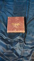 Closed square brown box with gold script, scratched surface
