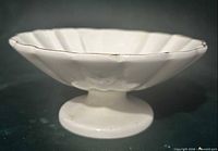 Side view showing pedestal base, scalloped bowl, rim chips and gold trim wear