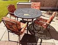 round cast aluminum table with four cushioned chairs outdoors