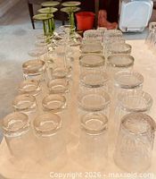 Various sizes of inverted clear crystal tumblers with starburst bases alongside green-stem wine glasses