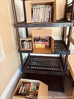Four-tier plastic shelf holding three open boxes of assorted VHS, DVD and CD media