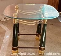 Angled view of glass-top end table showing brass finials, dark green legs, brass collars and foot rings