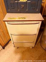 front view of off-white metal cabinet showing three drawers and laminate top