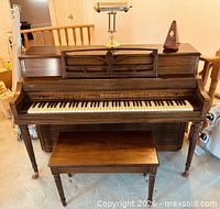 Front view of Hardman, Peck & Co. upright piano with bench and brass lamp