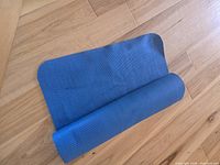 Blue PVC yoga mat partially rolled on wooden floor