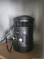 Front angled view of Pelonis cylindrical black space heater showing brand label, control knobs, power cord, and overall condition