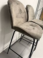 Two gray velvet counter stools side view showing metal legs and wear