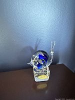 Full view of glass snail figurine on base showing blue accent and overall form