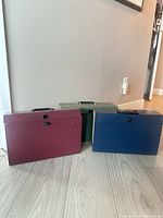 Three boxes—burgundy, green, navy—front view showing latch closures and handles