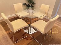 Dining set showing glass table and four beige chairs in lit room