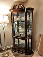 Full front view of corner curio cabinet showing glass front door, cherry finish, interior contents for scale