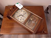 Full view of wooden Beacon wall clock on table showing dial and lower glass door