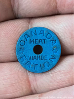 Obverse of blue Canadian meat ration token held between fingers showing full text and center hole