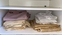 Folded mauve, cream, white sheer, beige and gold curtain sets on shelf