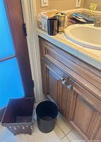 Square decorative metal waste bin and black cylindrical waste bin beside bathroom vanity