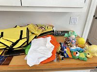 Overview of backpack, towel, clothing, plush toys, ceramic bells and ball on tabletop