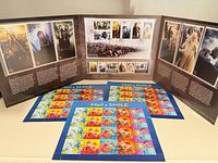 Front view of three Lord of the Rings tri-fold packs standing and three Pixar Mail a Smile stamp sheets laid flat