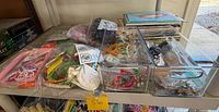 Shelf with clear drawer organizers containing craft supplies; craft books stacked and lined along side