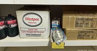 Shelf view showing Coleman propane cylinders, Westpac joint compound box, Philips blister bulb and two Feit Electric bulb boxes