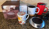 Full lot showing Sweetfull boxed warmer, Brookstone warmer, boxed tumbler, three mugs