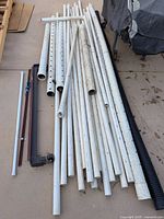 Group of PVC pipes, black corrugated pipe, metal rails and thin white rod on ground
