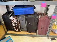 Five upright suitcases (black, floral, gray, black, maroon) with blue suitcase resting on top