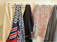 Four garments hanging: off-white poncho, navy patterned poncho, black poncho, sheer floral jacket