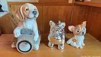 Front view of three dog figurines including beagle with lantern, chrome terrier, ceramic chihuahua