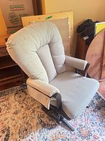 Front-angled view of grey upholstered Dutailier glider chair showing seat, back, arms and base