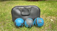 Three blue/black lawn bowling balls and black carry bag on grass