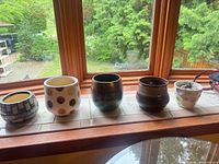 All five pottery flower pots lined on windowsill showing designs and relative sizes