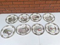 All eight dinner plates laid out face up showing assorted scenes and border design
